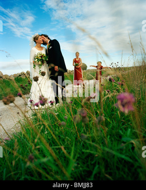 Scandinavia, Sweden, Oland, Bride and groom kissing with bridesmaid and flower girl in background Stock Photo