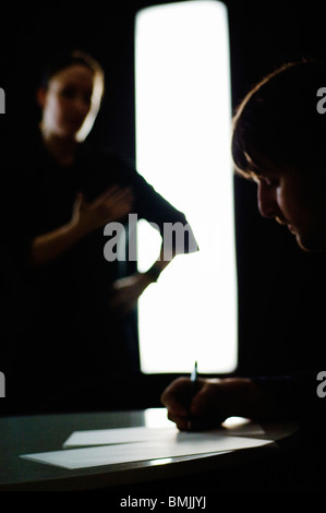 Man and woman silhouetted. Woman standing. Man seated, writing on paper at desk Stock Photo