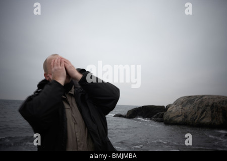 Scandinavia, Sweden, Bohuslan, Man standing by sea, hands covering face Stock Photo