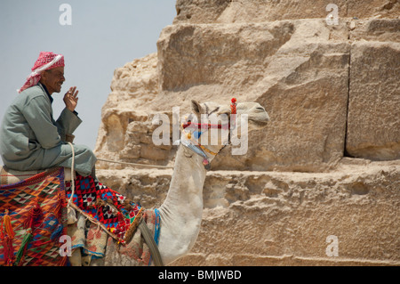 Egypt, Cairo. Egyptian man in traditional attire on camel in front of The Great Pyramids of Giza. Stock Photo