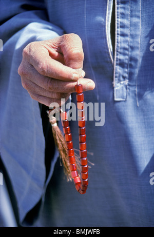 In Aswan, Egypt, a close-up of a man's hand holding a string of red prayer beads and wearing a blue galabeya. Stock Photo