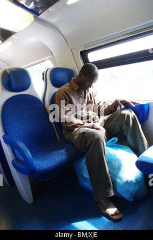 Immigrant in urban train sleeping on armchair with his bag of goods to sell.  Rome Italy Stock Photo