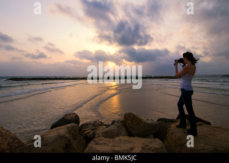 A woman take a photo at sunset in Frishman beach at the Mediterranean seashore of Tel Aviv in Israel Stock Photo