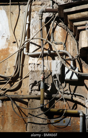 electricity power wiring circuit cables tubes on side of property wall in sun Stock Photo