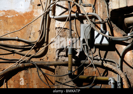 electricity power wiring circuit cables tubes on side of property wall in sun Stock Photo