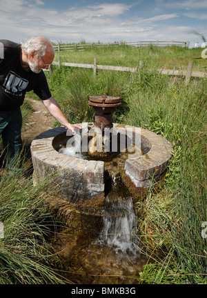 Man taking a drink from an Artesian Aquifer at Harty Ferry, Kent, England, UK. Stock Photo