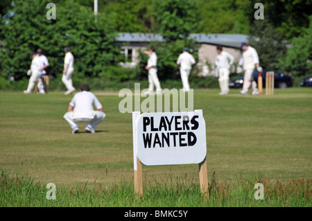 Village green competitive amatuer summer cricket match in progress and advertising sign for players wanted Navestock Brentwood Essex England UK Stock Photo