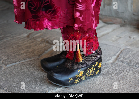 The feet of a local woman in a Bokhara market in Uzbekistan wearing traditional national dress with embroidered clogs. Stock Photo