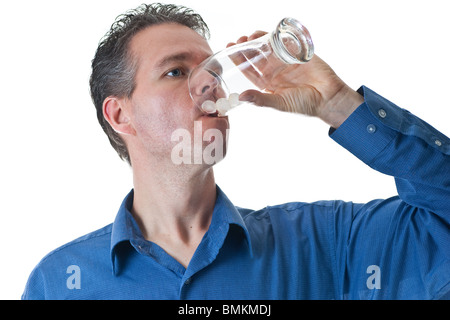 A man in a blue dress shirt, finishing a drink of pop from a glass with ice, isolated on white. Stock Photo