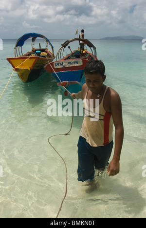 Young man pulls boats at coast in turquoise Indian Ocean. Havelock Island. Andaman Isles. India. Stock Photo