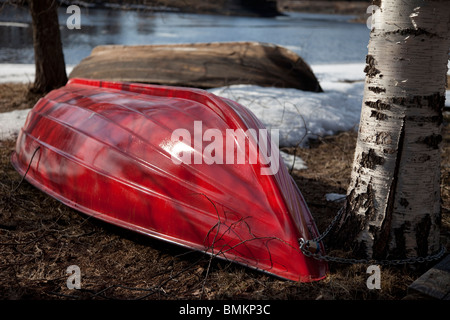 Upturned small red fiberglass rowboat / skiff / dinghy at early Spring , Finland Stock Photo