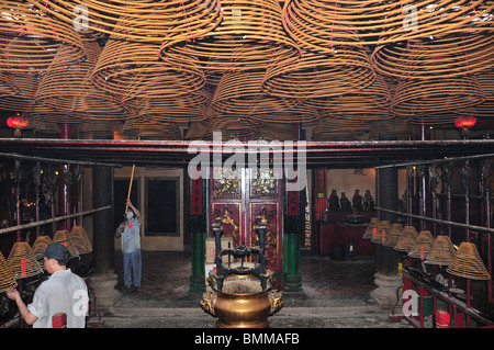 Workmen attending incense cones hanging from the ceiling inside the entrance to the Man Mo Temple, Sheung Wan, Hong Kong Stock Photo