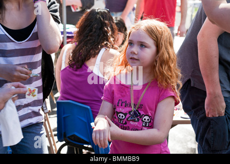 pretty little red haired girl waits expectantly for tattoo at face painting booth at Ninth Avenue International Food Festival Stock Photo