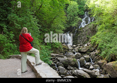 a woman taking a photograph of Torc Waterfall, Killarney National Park, Co. Kerry, Republic of Ireland Stock Photo