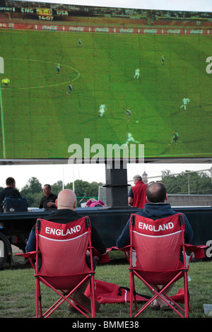 Two England fans sitting in chairs watching the England vs United States football game at the 2010 World Cup on a giant screen. Stock Photo