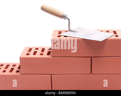 Stainless steel trowel laying on unfinished brick wall isolated on white Stock Photo