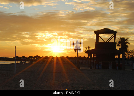 Watchtower and parasols on the beach at sunset, Puerto Cabopino, Marbella, Costa del Sol, Malaga Province, Andalucia, Spain. Stock Photo