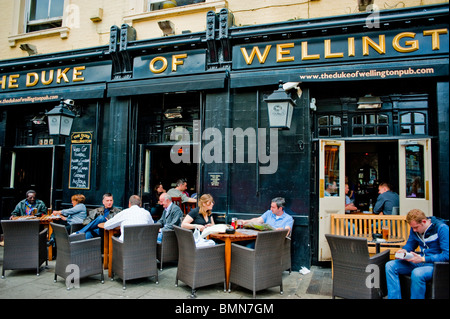 London, England, UK, Medium Crowd people Sharing drinks on Portobello Road District, Outside Street , Traditonal English Pub, 'The Duke of Wellington', sign in Front Stock Photo