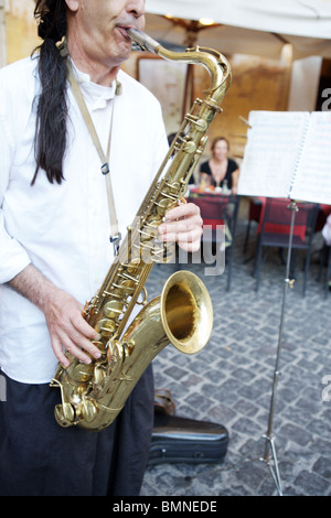 One man play music with a saxophone in the street in front of Rome Italy restaurant with tourists eating dinner. Stock Photo
