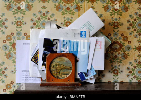 old letters stacked in letter rack on dusty shelf against old stained wallpaper Stock Photo