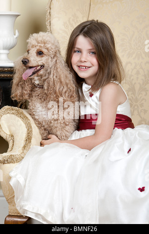 Shot of a Happy Blonde Girl in Large Armchair with an Apricot French Miniature Poodle Stock Photo