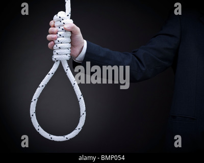 A man on a suit holds a hangman's noose over a gray background. Stock Photo