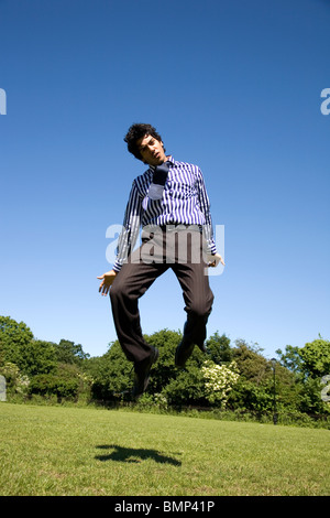 Man is business clothing jumping in the air in Park Stock Photo