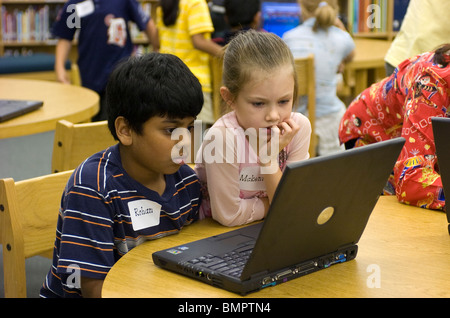 Indian boy and Anglo girl look at laptop computer in elementary school library in Austin, Texas, Stock Photo