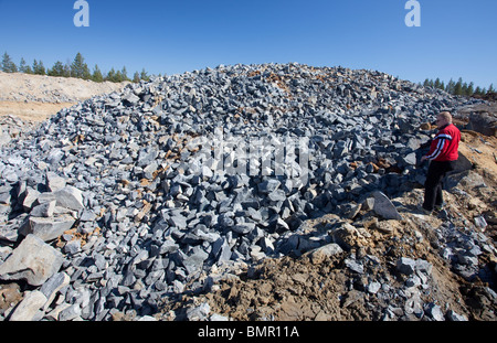 Man watching pile of rocks that were exploded from the bedrock at rock quarry , and later used as raw material , when manufacturing gravel , Finland Stock Photo