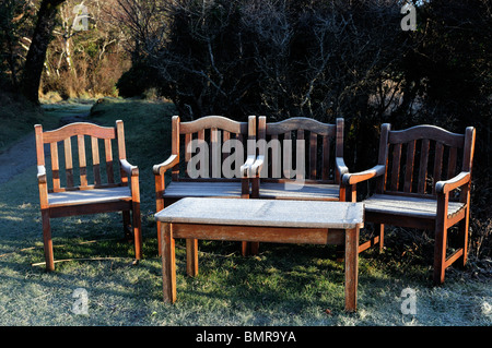 ice frost covered garden furniture wooden seat bench winter cold hedge seat chairs table seating early morning light sunrise Stock Photo