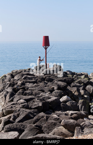 one man fishing off Rock stone groynes sea defences at Barton on Sea Stock Photo