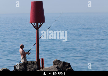 one man fishing off Rock stone groynes sea defences at Barton on Sea Stock Photo