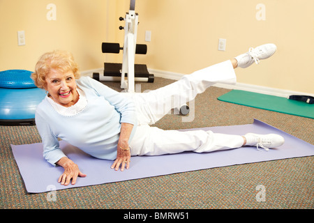 Fit happy senior woman doing stretching exercises on her yoga mat. Stock Photo