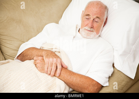 Senior man sound asleep on the couch, suffering from a cold. Stock Photo