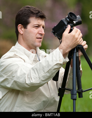 Young man using camcorder on a tripod outdoors in a forest Stock Photo