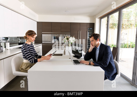 Couple looking at laptop and ipad in their high-tech kitchen. Stock Photo