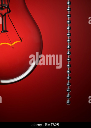 Close up on a transparent light bulb with a pull switch over a red background. Stock Photo