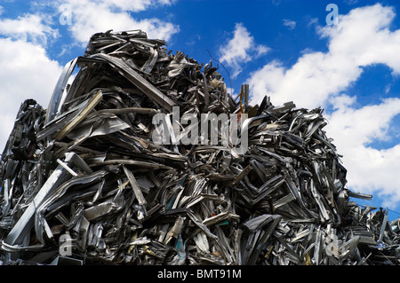 Scrap aluminum has been crushed, baled, and piled high with a clean blue sky with white clouds overhead. Stock Photo