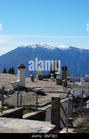 View over rooftops towards snow capped mountains of the Sierra Nevada, Capileira, Las Alpujarras, Granada Province, Spain.