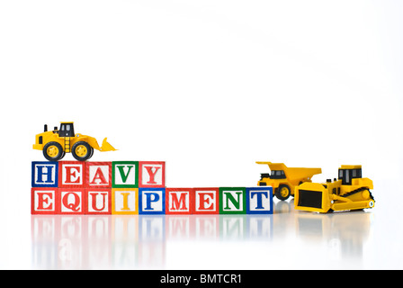 Colorful children's blocks spelling HEAVY EQUIPMENT with small construction machines - bulldozer, dump truck and front-end loade Stock Photo