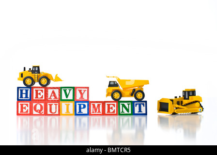 Colorful children's blocks spelling HEAVY EQUIPMENT with small construction machines -bulldozer, dump truck and front-end loader Stock Photo