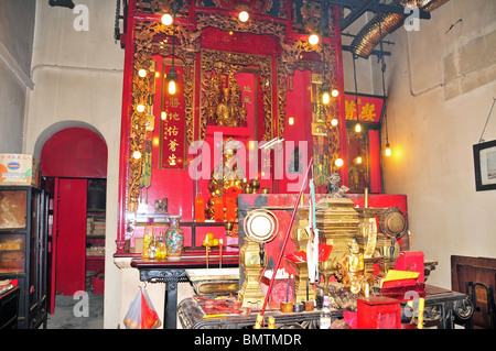 Red altar and gold buddhist statues in the brightly lit interior of the Pak Sing Ancestral Hall, Sheung Wan, Hong Kong Stock Photo