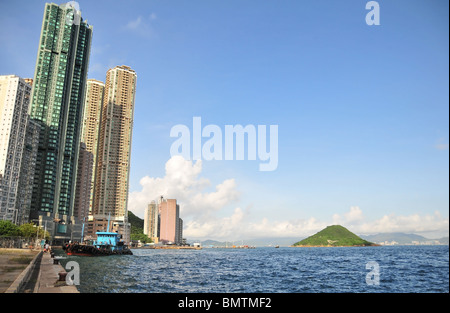 Blue sky view of dangerous cargo tugboat at stone wharf below skyscrapers of Kennedy Town, west end Victoria Harbour, Hong Kong Stock Photo