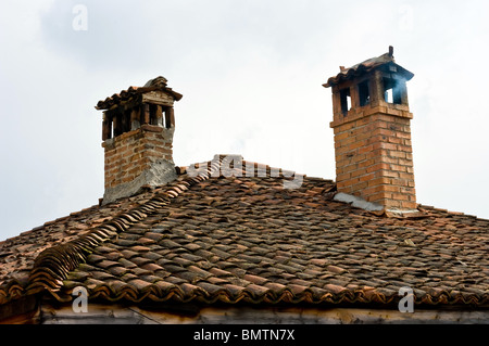 Tiled roof of an old house. Chimney smoke. Stock Photo
