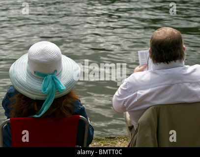 A man and a woman, a couple, a lady with a fancy straw hat sat by the River Thames, Marlow, Bucks UK Stock Photo