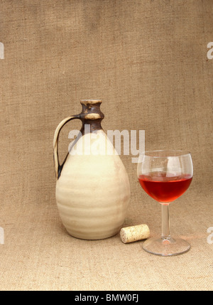 Still life with a clay bottle and wineglass on burlap background Stock Photo