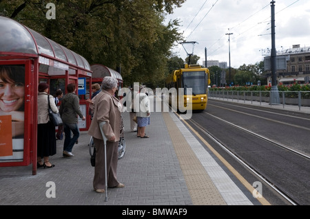Polish people waiting at a tram stop with yellow tram approaching, Public transport, Warsaw, Poland, EU Stock Photo