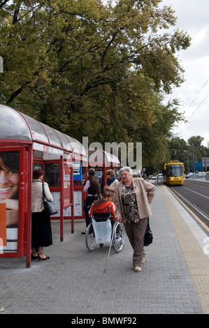 Polish people waiting at a tram stop with yellow tram approaching, Public transport, Warsaw, Poland, EU Stock Photo