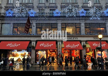 Hamleys toy shop store brand logo on window blinds winter dusk busy with Xmas shoppers in Regent Street West End Christmas light decorations London UK Stock Photo