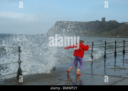 young girl plays daredevil as waves crash over the seafront, Royal Albert Drive, Scarborough, North Yorkshire, England, UK Stock Photo